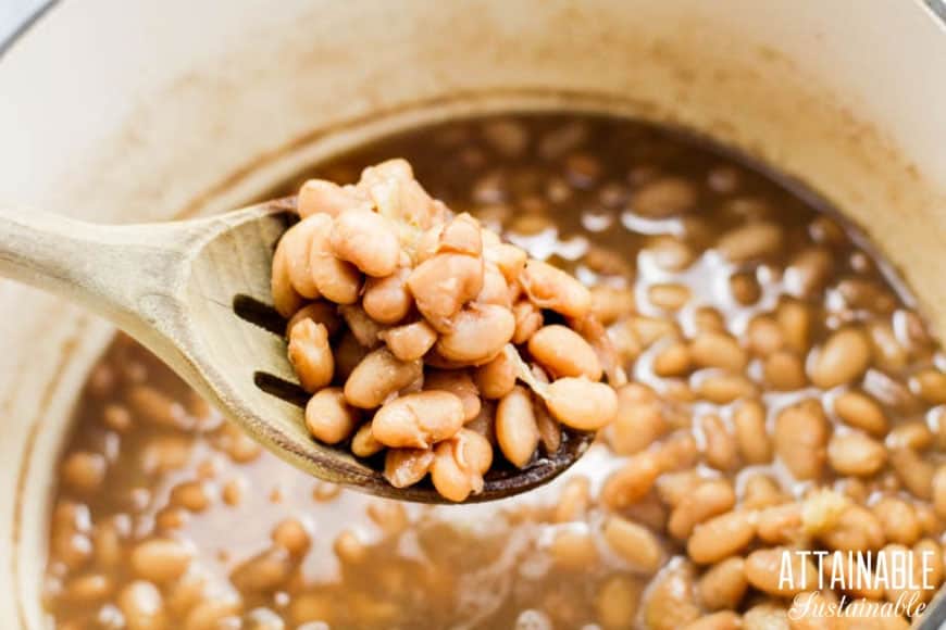 pinto beans cooked in a white pot, with some on a wooden spoon