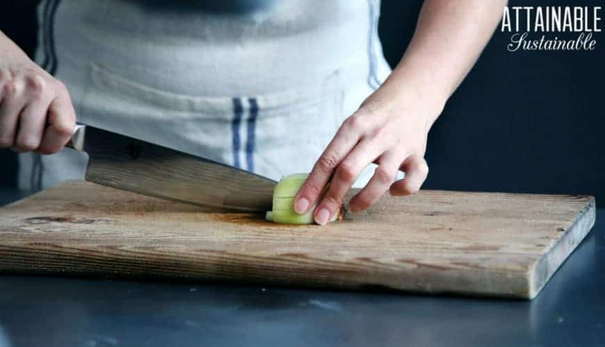 two hands with a knife cutting on onion on a wooden cutting board - must have cooking skills