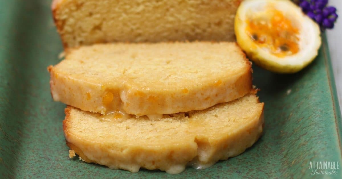 LOAF OF yellow cake on a green rectangular plate with a half lilikoi and purple flower in the background