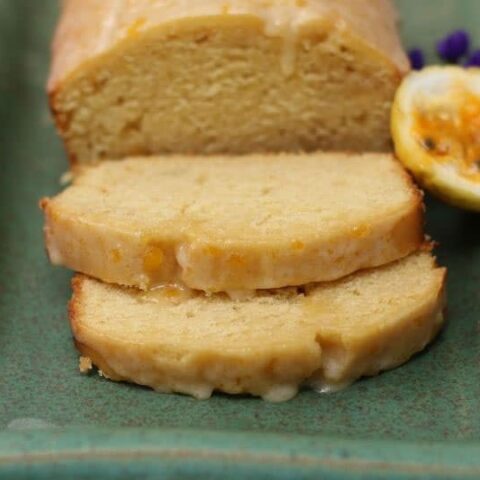 LOAF OF passion fruit cake on a green rectangular plate with a half lilikoi and purple flower in the background