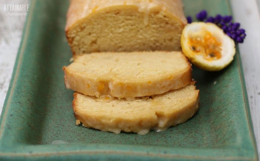 LOAF OF passion fruit cake on a green rectangular plate with a half lilikoi and purple flower in the background