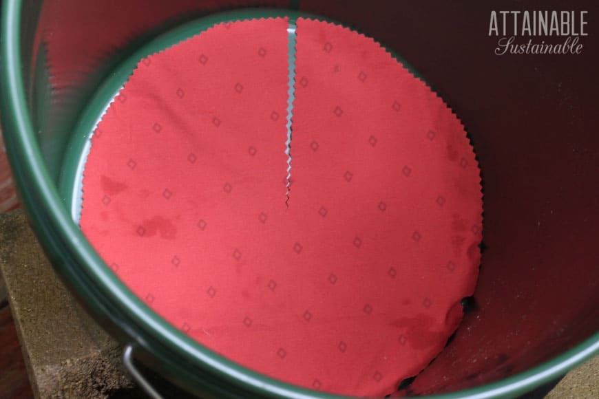 round piece of red fabric in the bottom of a bucket to make an upside down tomato planter