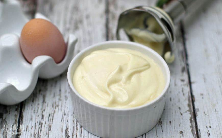 homemade mayonnaise in a white dish, with a brown egg and a stick blender