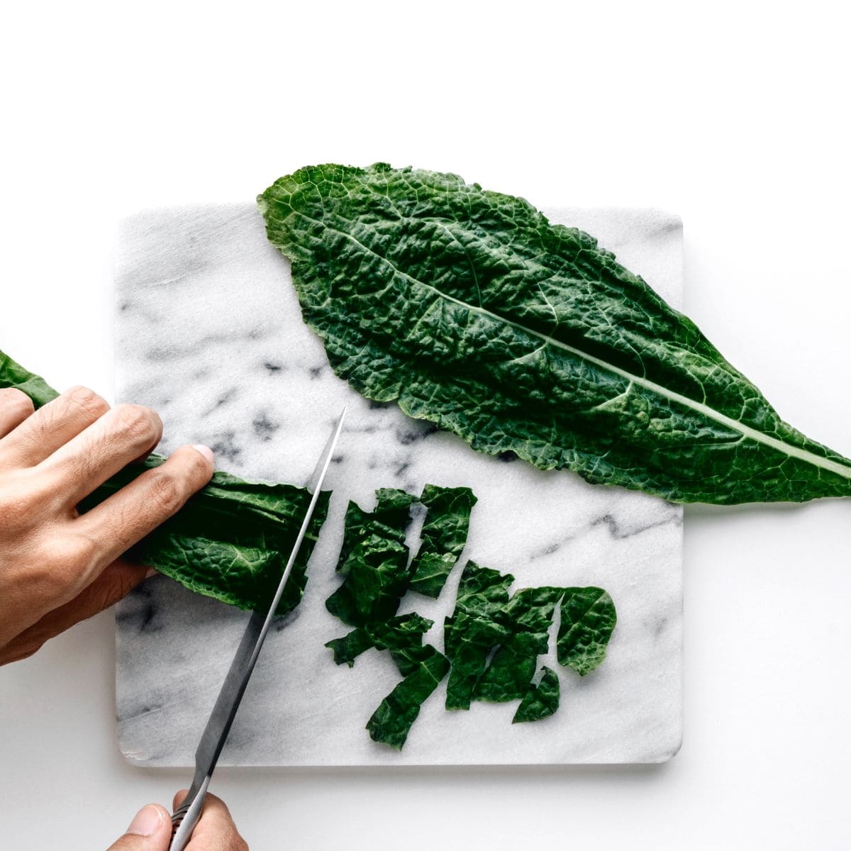 hand cutting kale leaves on a marble surface.