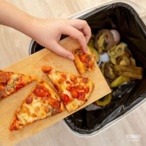 hand scraping slices of pizza off a cutting board into the trash.