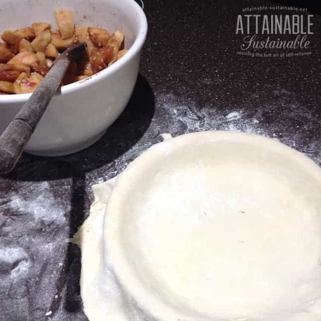 white bowl full of apple pie filling with apple pie crust on a floury countertop - ready for making an apple pie recipe from scratch