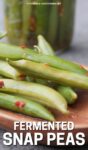 close up of fermented snap peas on a wooden tray, jar in the background.