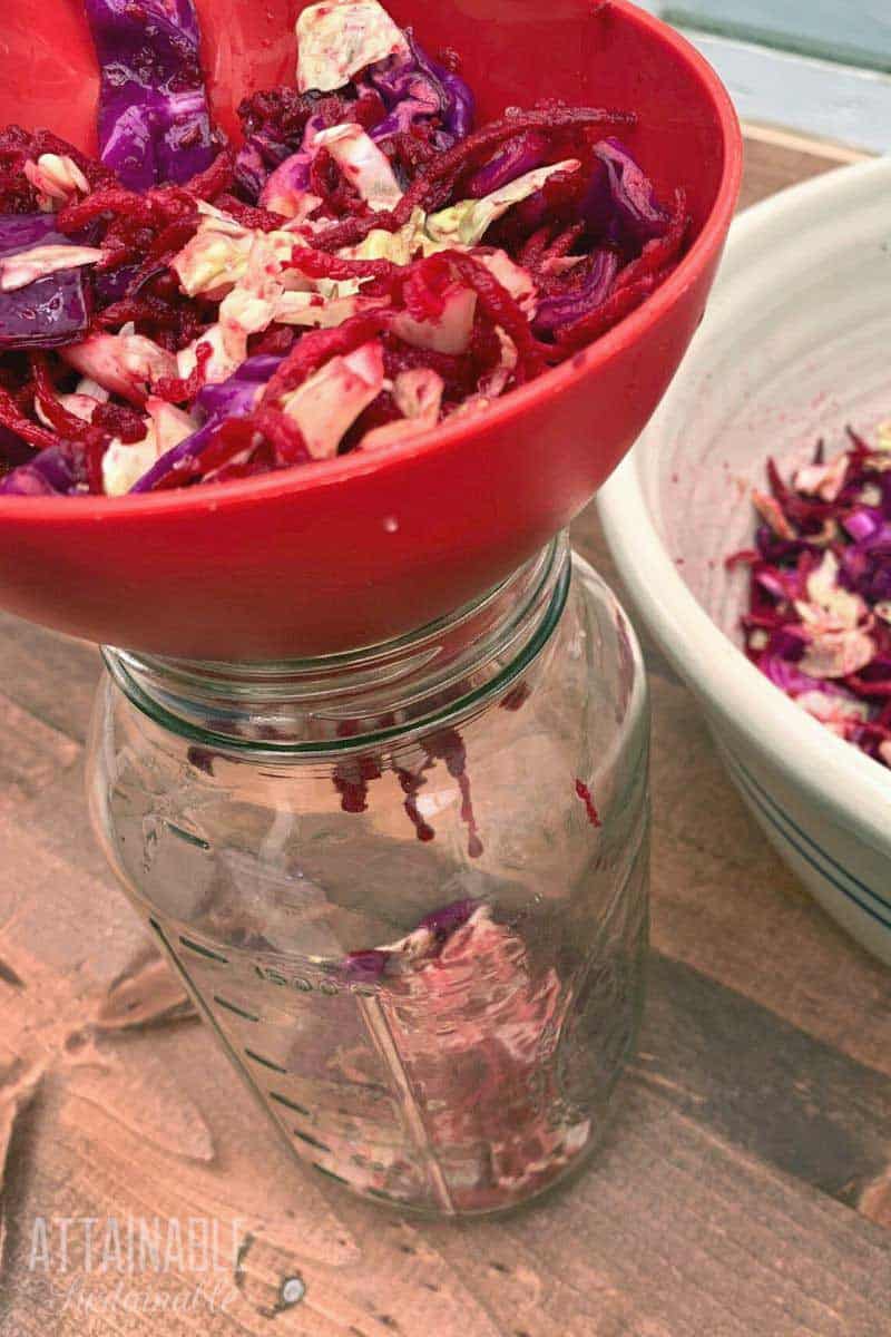 putting beet sauerkraut into a jar with a red funnel