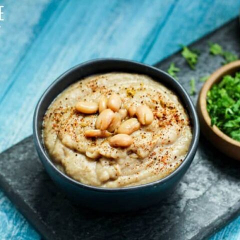 bowl of homemade refried beans with more bowls of cilantro and chopped onion on a teal background