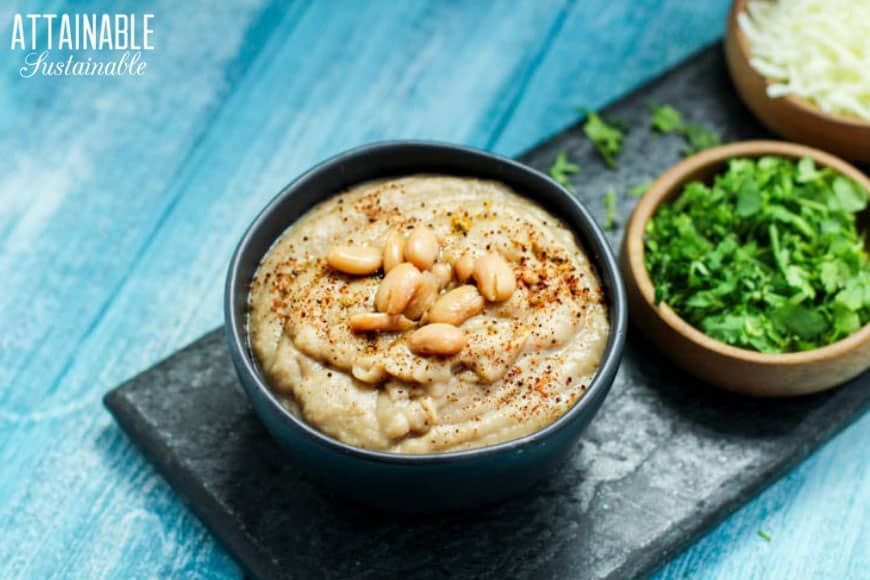 bowl of homemade refried beans with more bowls of cilantro and chopped onion on a teal background