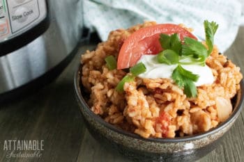 easy spanish rice in a brown pottery bowl with a tomato wedge and sour cream