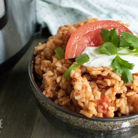 easy spanish rice in a brown pottery bowl with a tomato wedge and sour cream