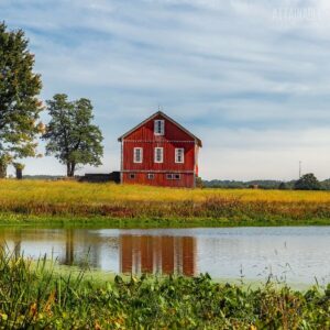 red barn in the distance against blue sky and clouds, with a lake in the foreground.
