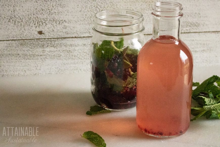 canning jar with berries and herbs behind a jar with infused vinegar