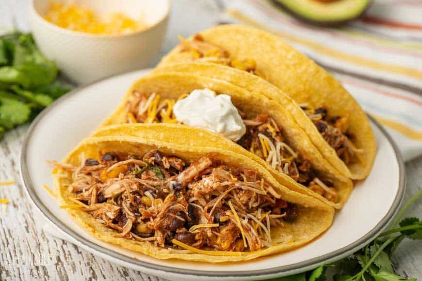 three shredded chicken tacos on a white plate