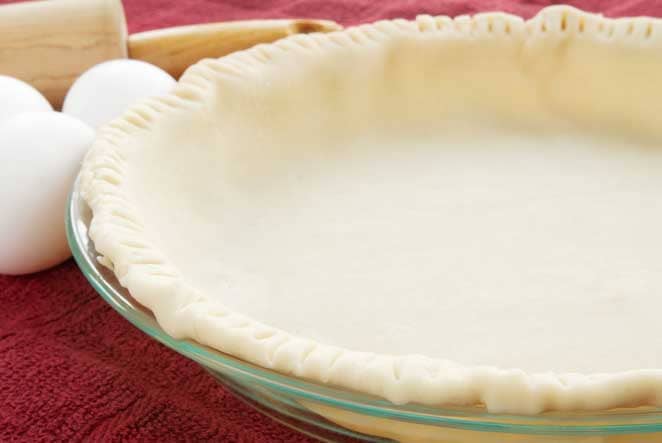 pie crust in a glass pie plate, eggs behind