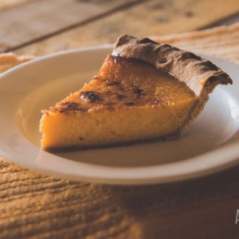 slice of pumpkin pie on a white plate (rough wood table)