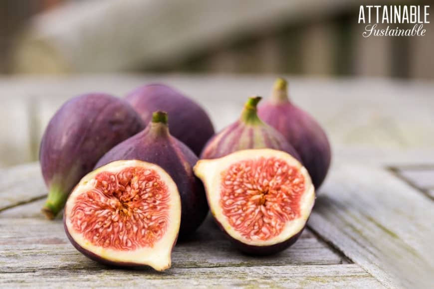 figs on a wooden table, one cut in half showing pinkish flesh