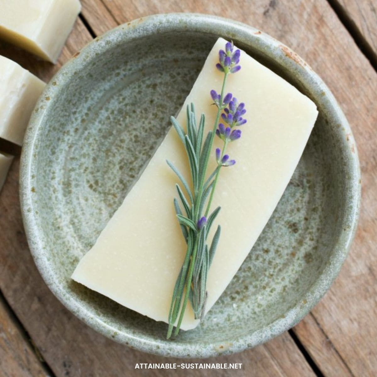 ivory colored bar of soap on a pottery dish, topped with a sprig of lavender.