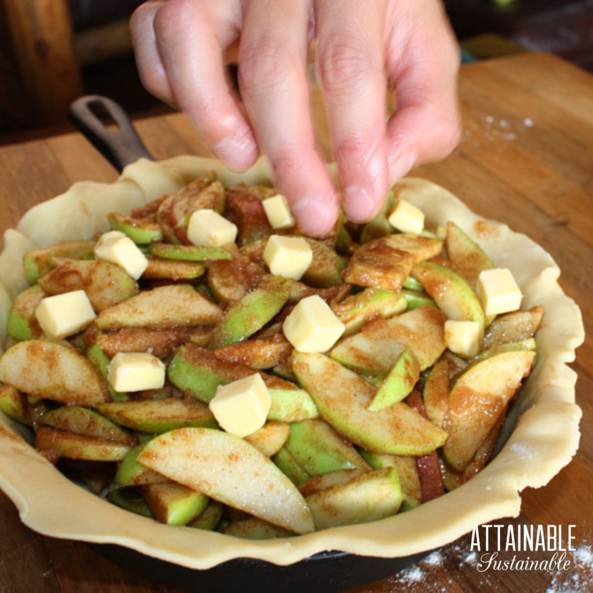 hand dropping pats of butter onto an uncooked pie.