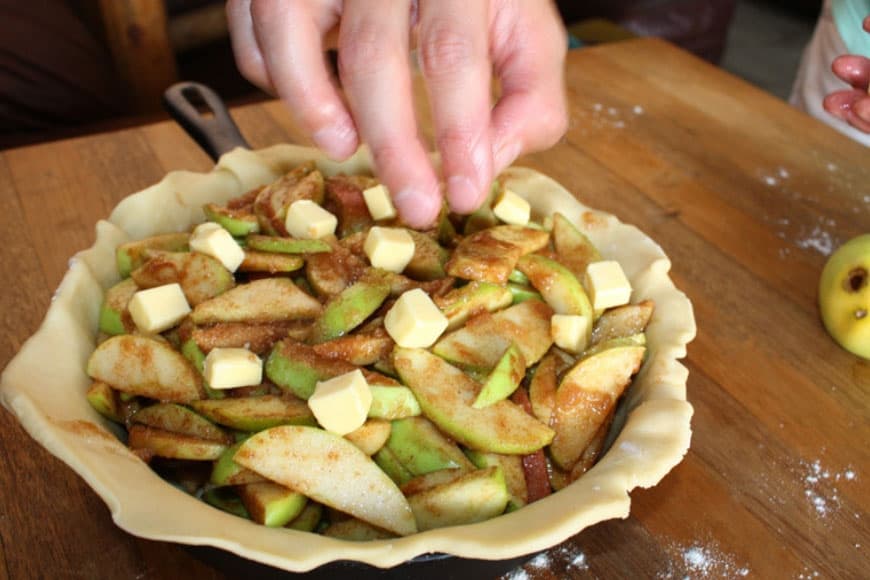 Pie crust in cast iron skillet filled with sliced of uncooked green apples and butter