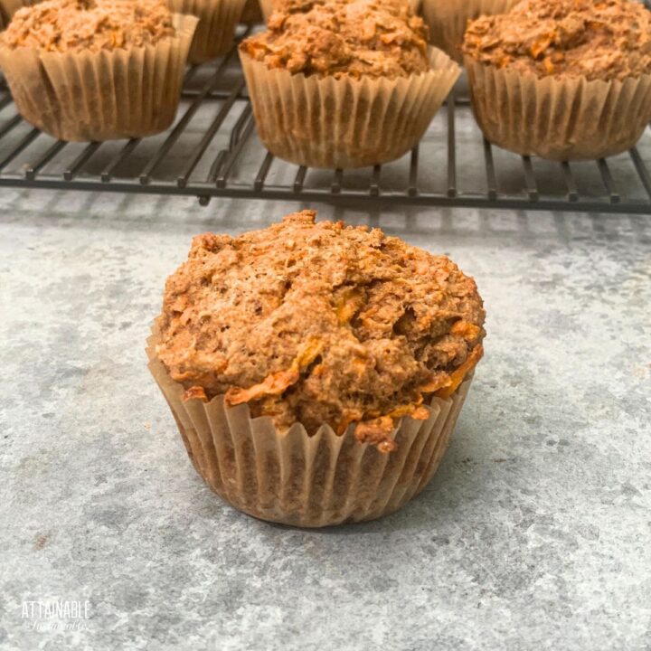 single sweet potato muffin with more in the background on a cooling rack.