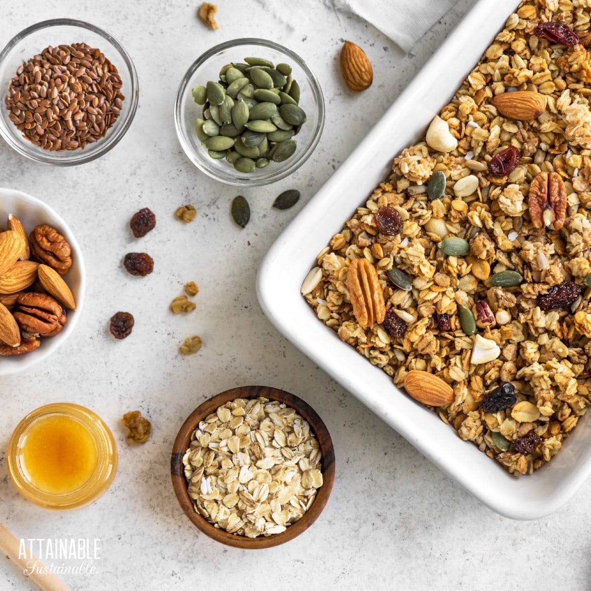 white pan of granola with ingredients in bowls around it.