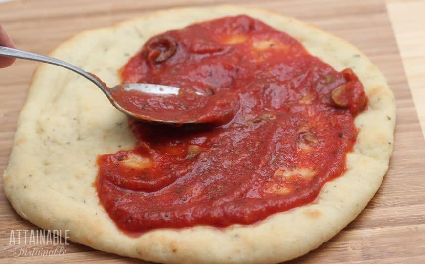 spoon spreading pizza sauce on dough.