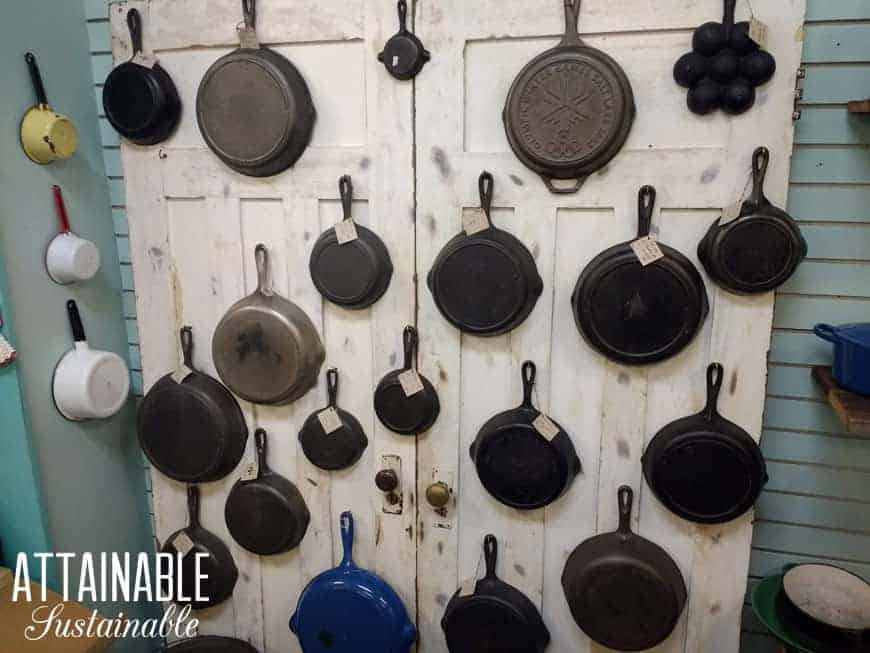 ~20 cast iron skillets hanging on a rustic white wall