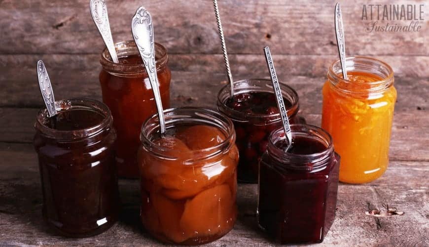 assortment showing difference between jams and jellies in glass jars, each with a metal spoon