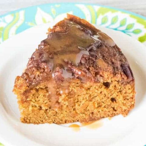 slice of applesauce cake with caramel sauce on a white plate with blue and green trim