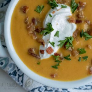 white bowl full of orange pumpkin soup, topped with sour cream and bacon.