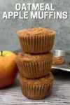 3 oatmeal apple muffins stacked, muffin tin and apple behind.