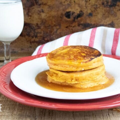 persimmon pancakes on a white dish with a red charger and a glass of milk