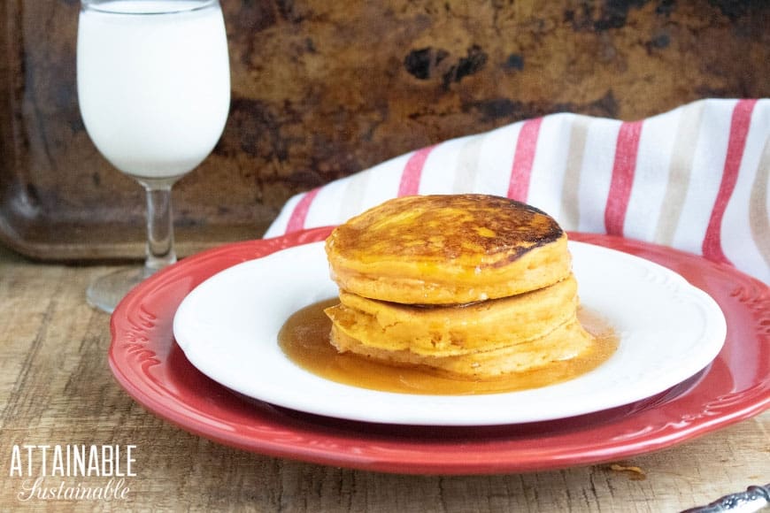 persimmon pancakes on a white dish with a red charger and a glass of milk