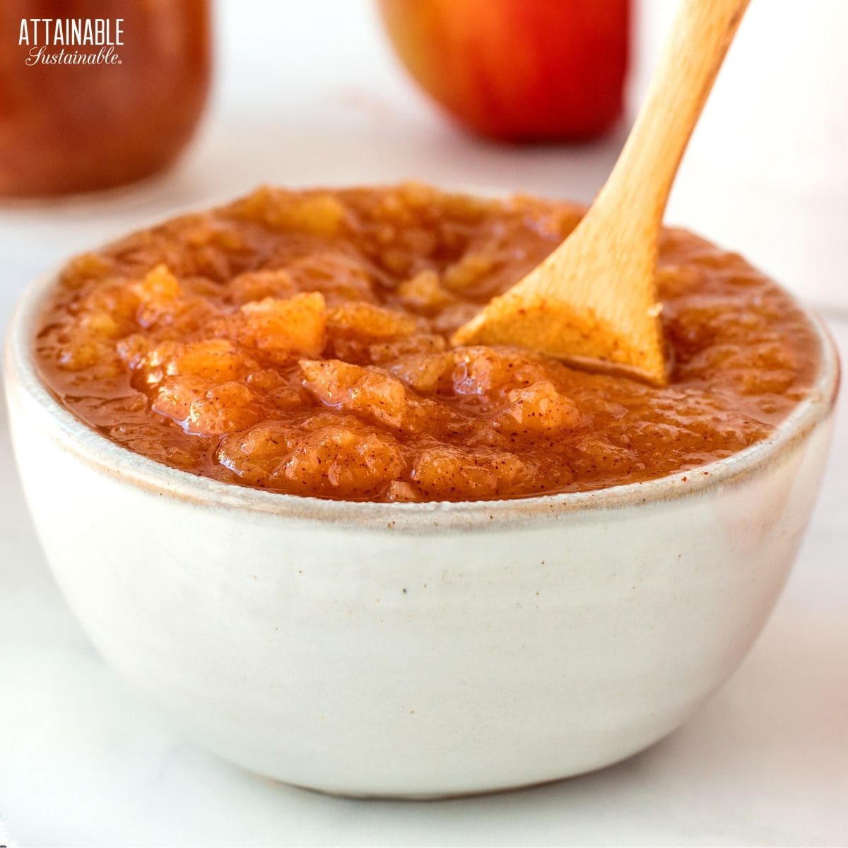 white pottery bowl filled with applesauce, a wooden spoon sitting in it.