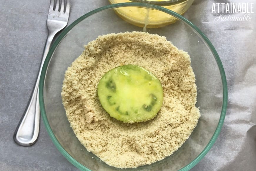 green tomato dipped in egg, sitting in a bowl of almond flour.