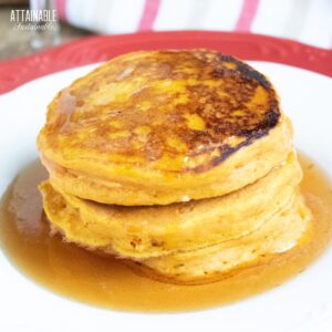 Persimmon pancakes on a white plate in a puddle of syrup.
