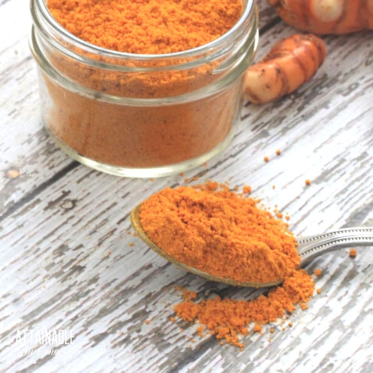 spoonful of orange turmeric powder, with a small jar full behind.