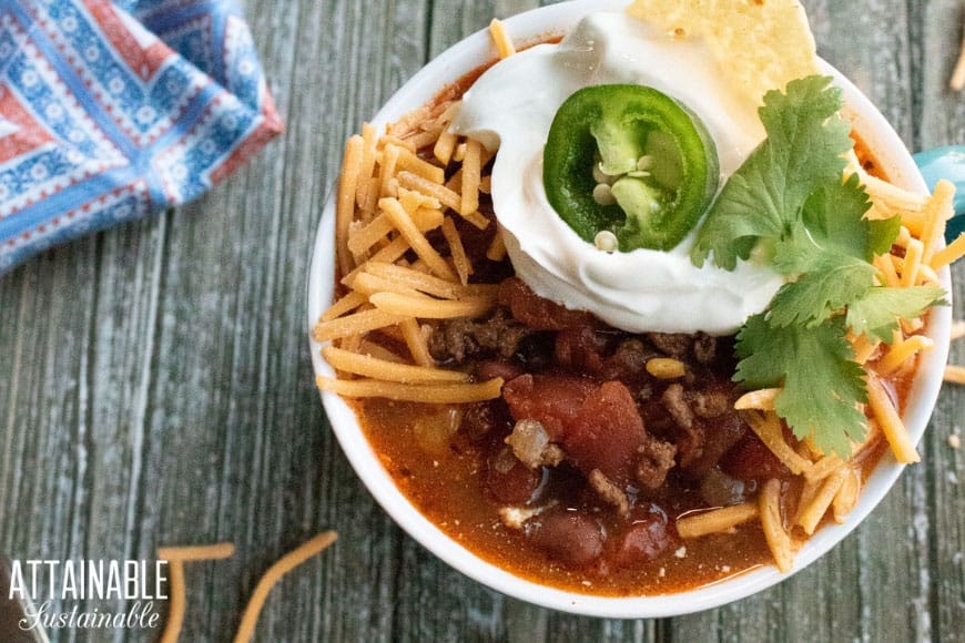 instant pot chili recipe in a teal, ribbed bowl with cheese, sour cream, jalapeno slice, and chip from above