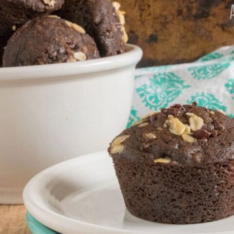 chocolate - chocolate chip muffin on a white plate, more in a white bowl behind.