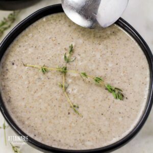brown bowl of cream of mushroom soup, with sprigs of fresh thyme.