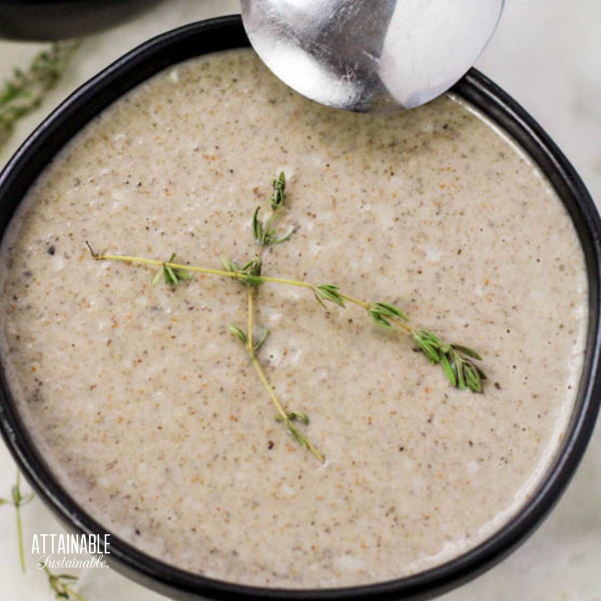 brown bowl of cream of mushroom soup, with sprigs of fresh thyme.