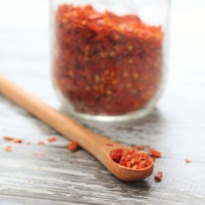 jar of homemade red pepper flakes, with some in a small wooden spoon.