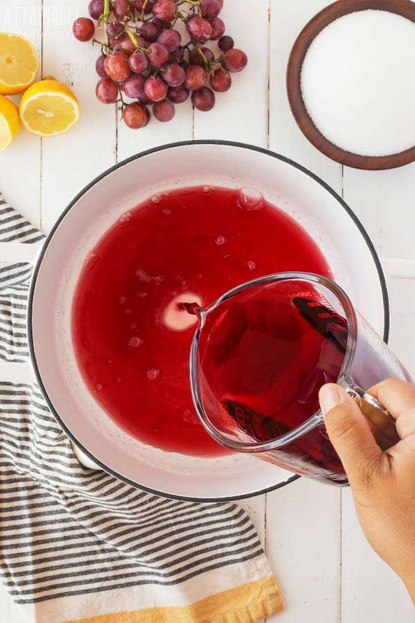 hand pouring grape juice from measuring cup into white porcelain pot