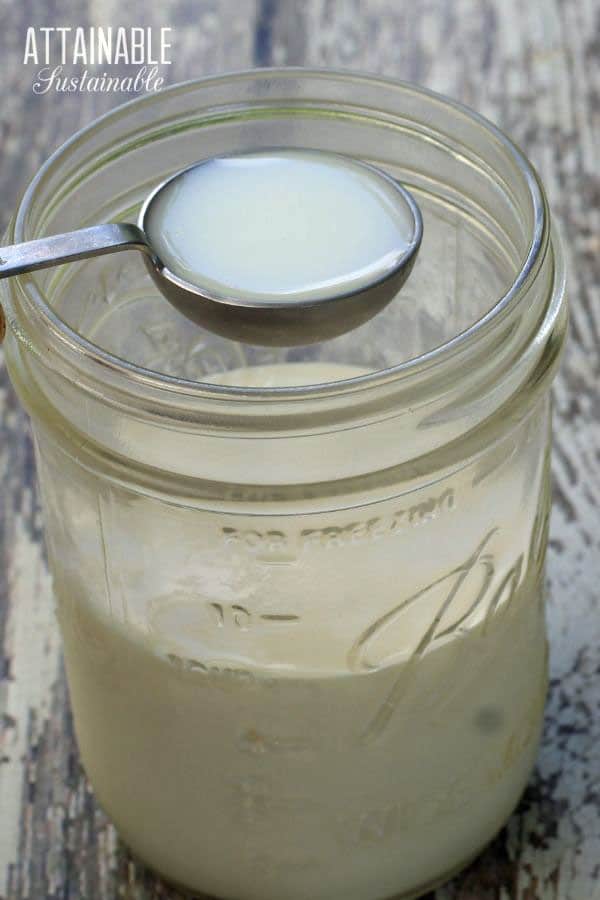 measuring spoon with buttermilk over a jar filled with heavy cream to make creme fraiche. 