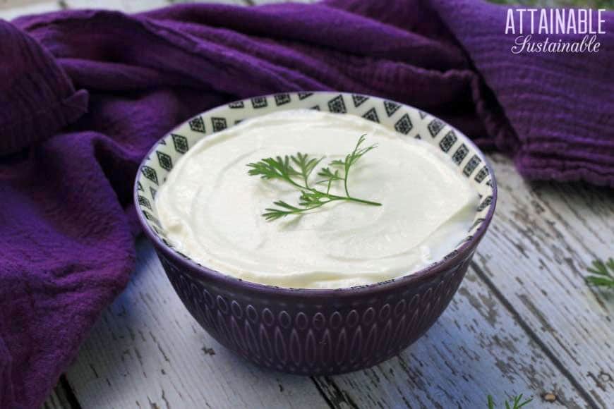 homemade sour cream in a purple bowl with an herb garnish