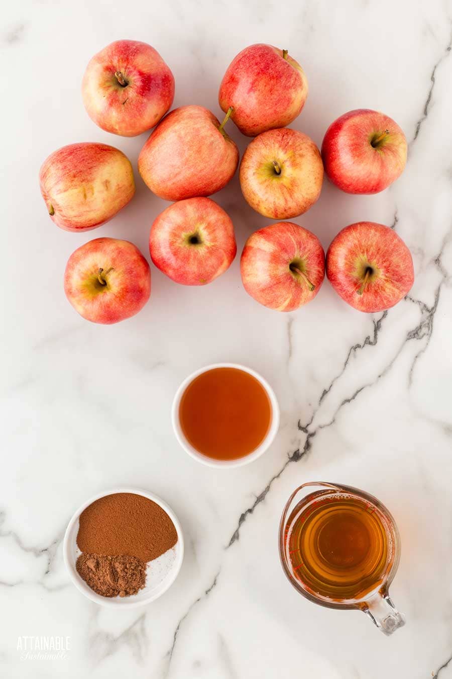 ingredients for making apple butter: red striped apples, apple cider, apple cider vinegar, and spices on a marble background.