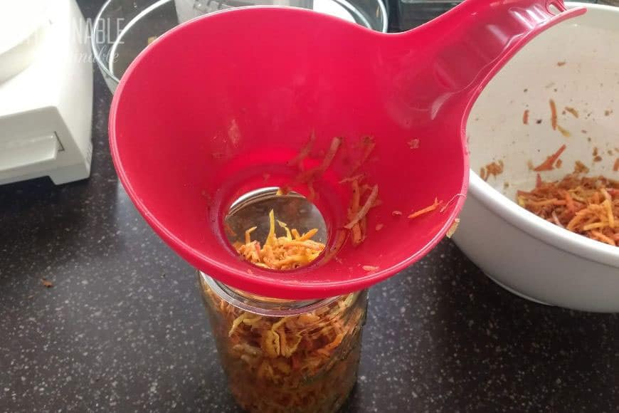 red canning funnel in a canning jar, partially filled with shredded carrots.