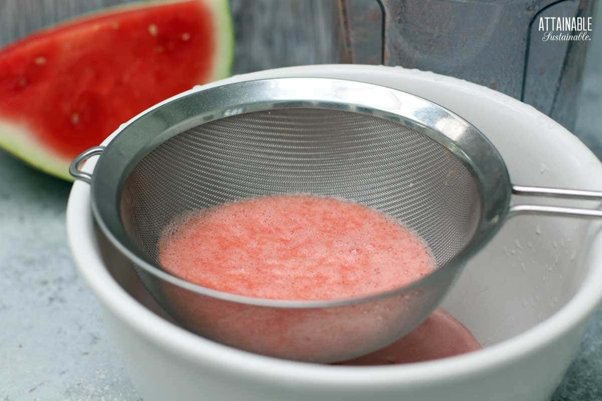 strainer with watermelon puree in it, over a white bowl.